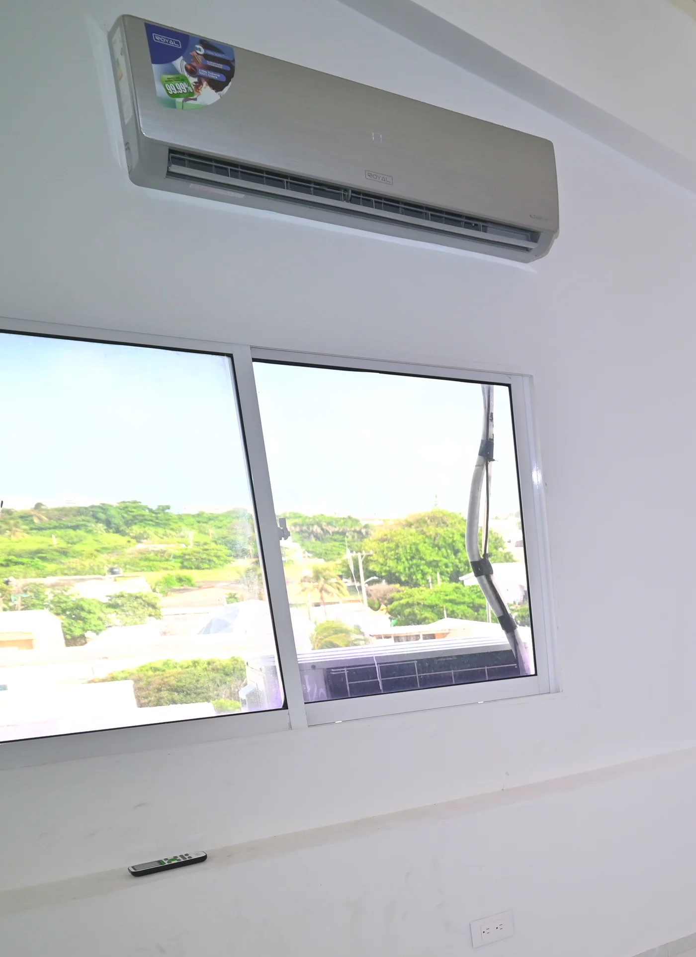 Aire acondicionado de pared sobre la ventana de una habitación, con el mando en el alféizar.