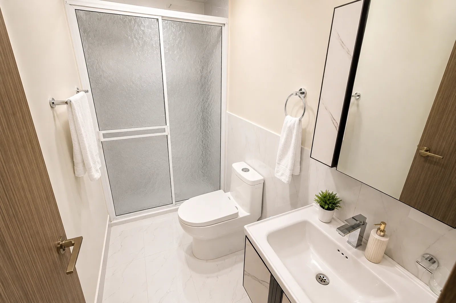 Baño con ducha de vidrio, lavamanos suspendido y toallas blancas.