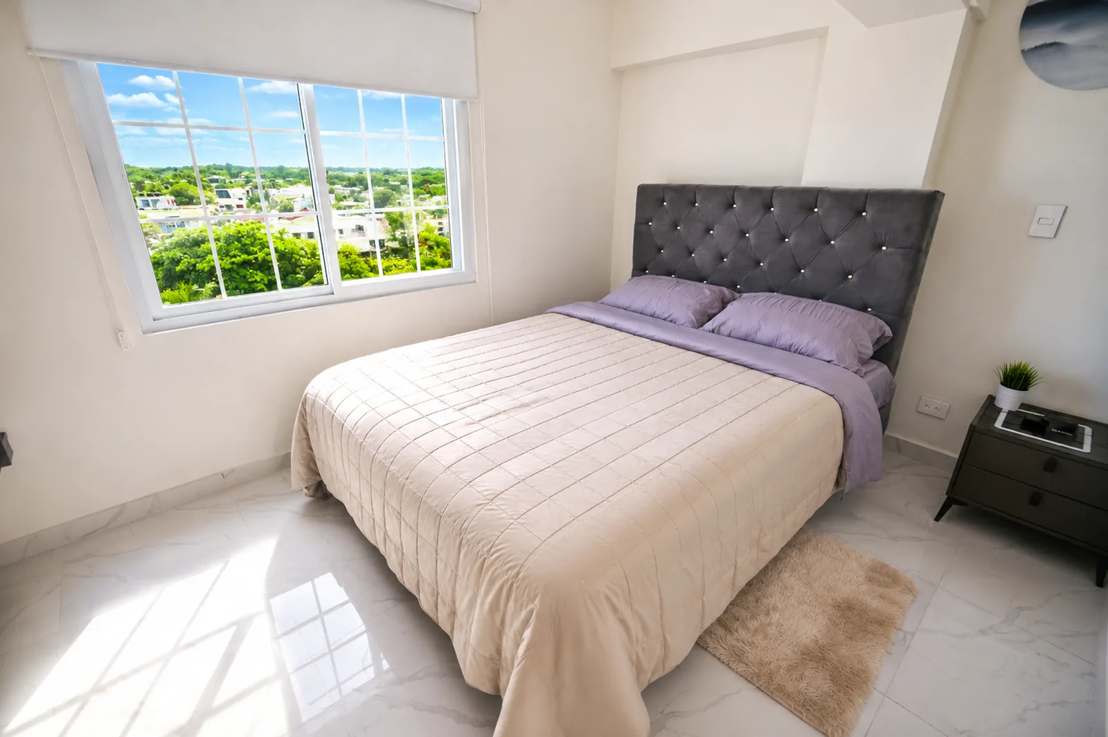 Cama junto a una ventana amplia con vista al verde y a los tejados de la isla.