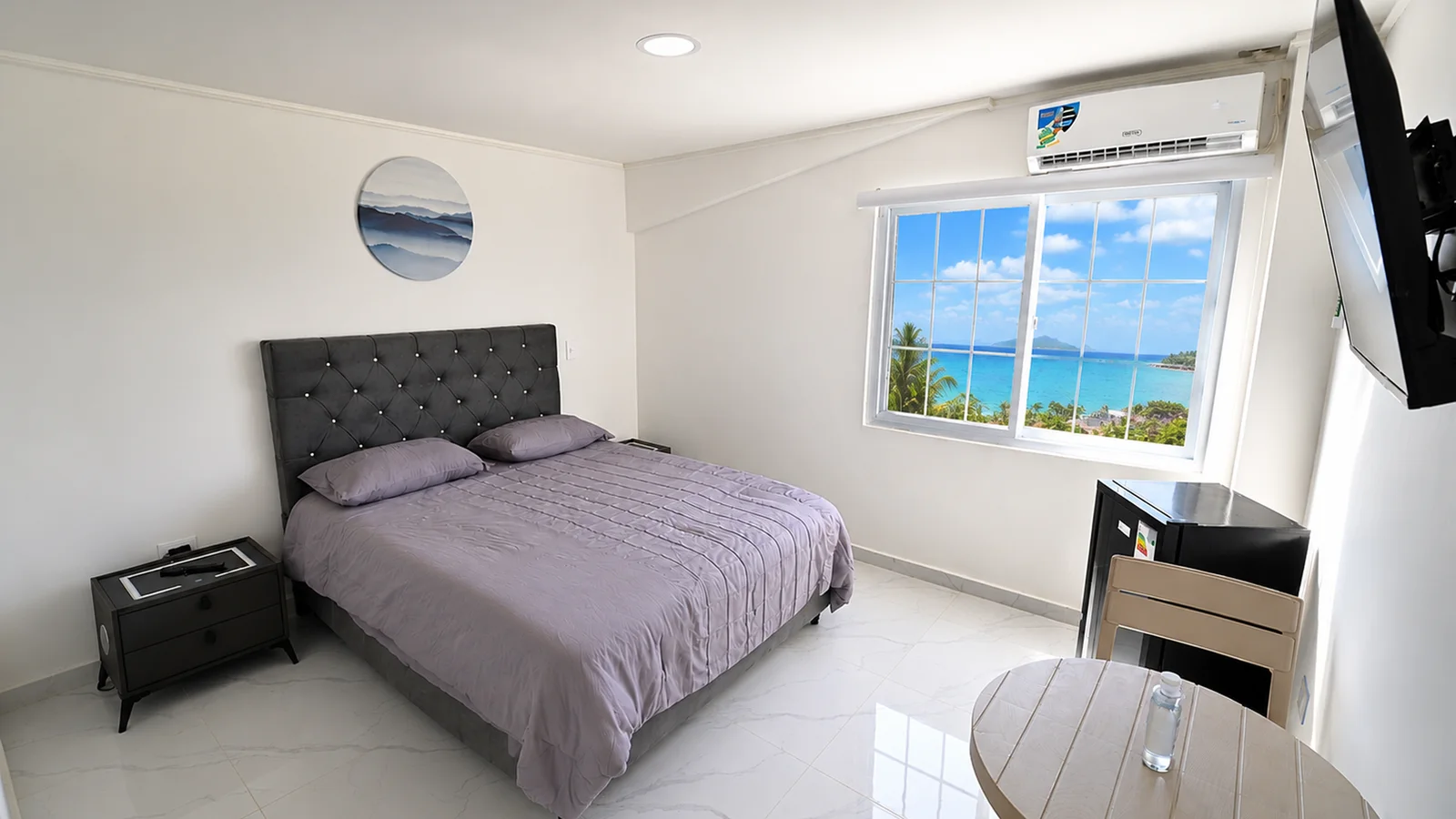La habitación desde la puerta, con la ventana abierta de par en par al mar turquesa.