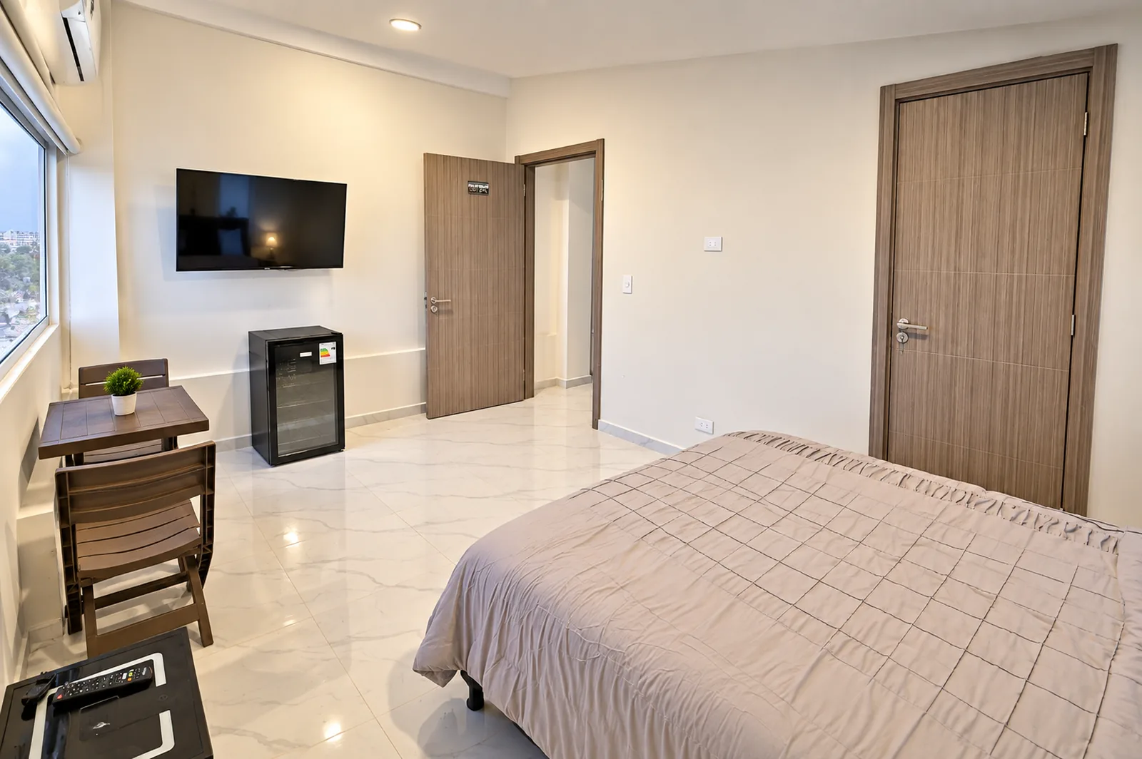 Habitación con cama doble, televisor de pantalla plana, minibar y una mesa plegable para dos junto a la ventana.