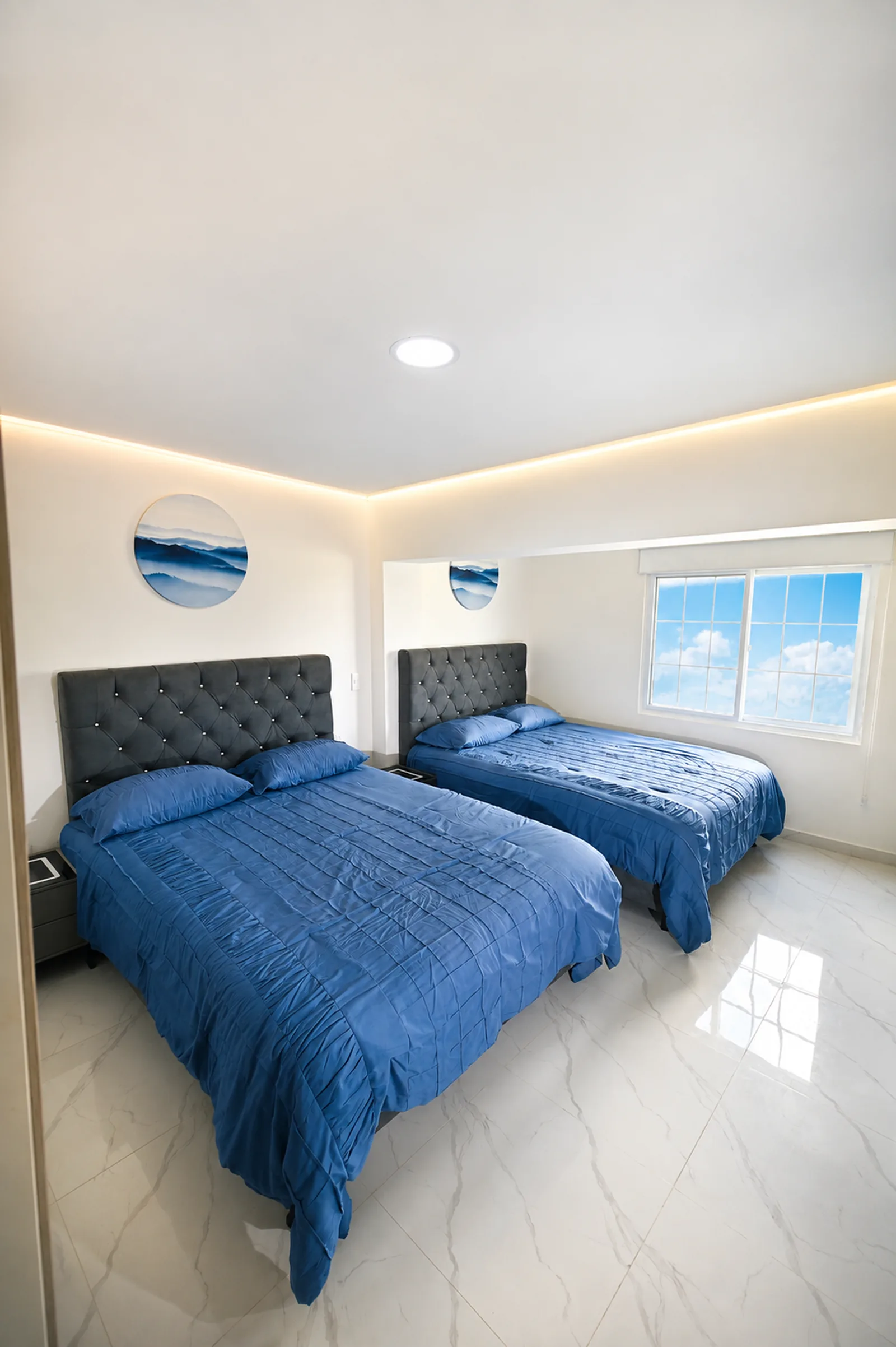 Habitación amplia con dos camas dobles vestidas en azul y luz indirecta en el cielo raso.