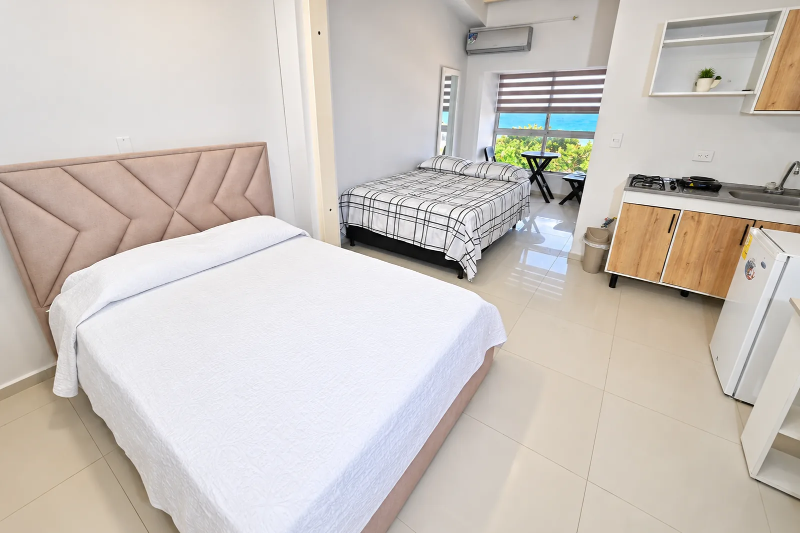 Estudio de vigas amarillas con cama doble, closet de madera y ventana con vista al mar.