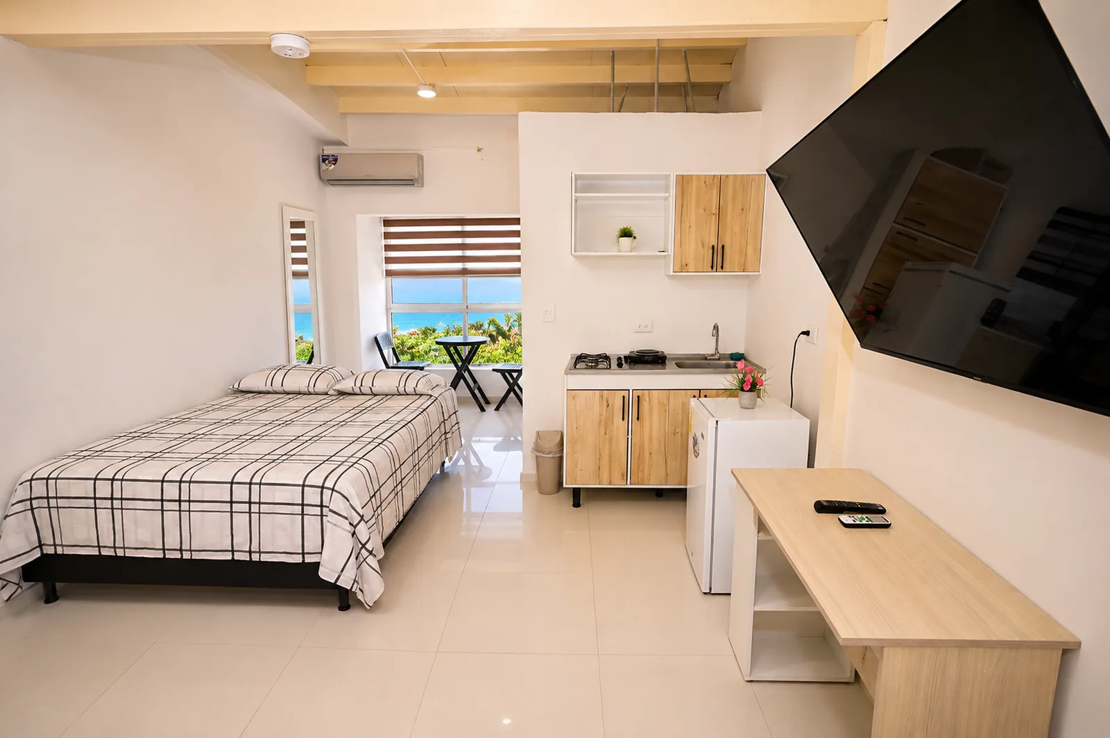 Estudio con cama doble, cocineta de dos puestos, nevera, escritorio y ventana con vista al mar.