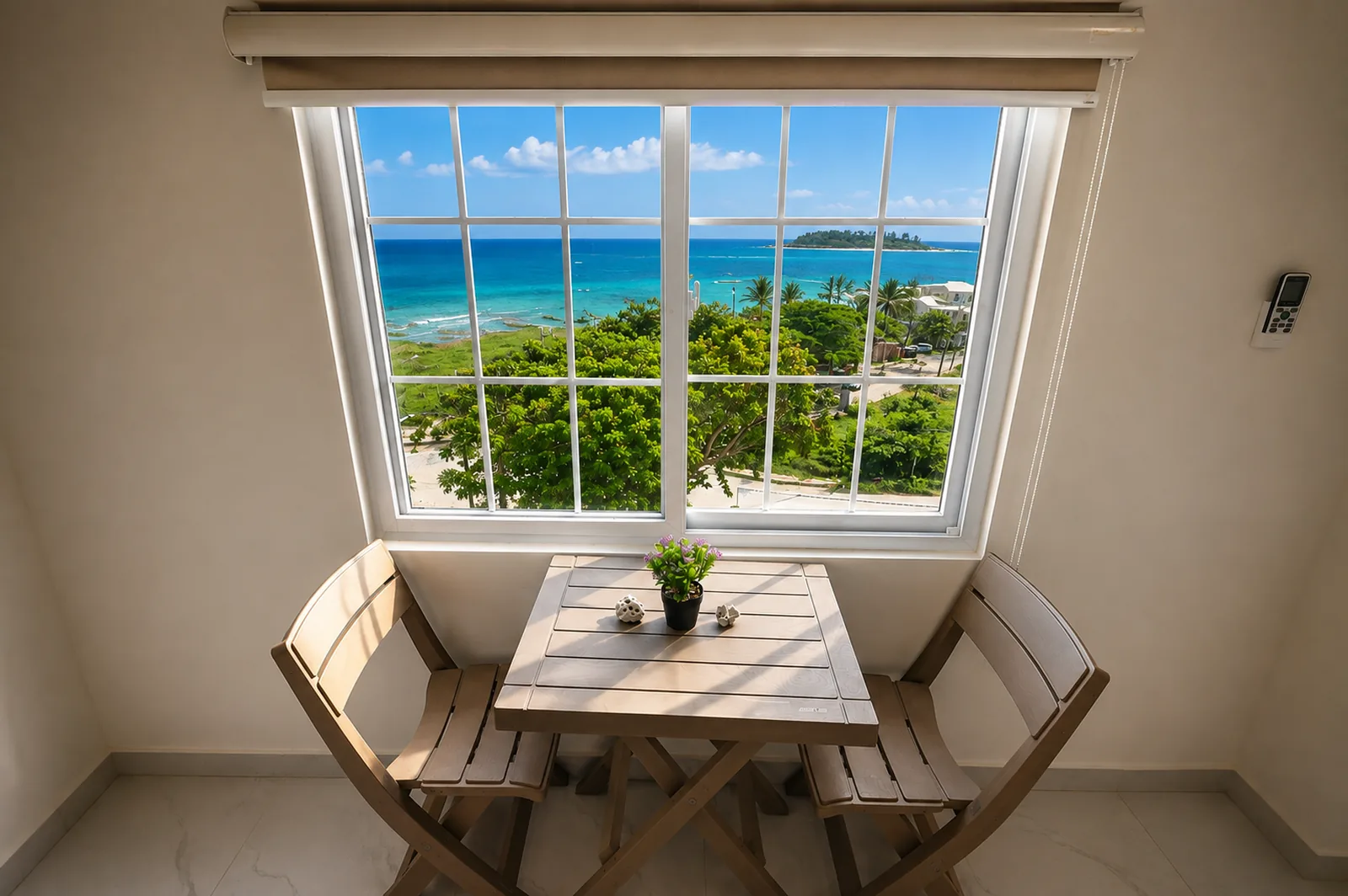 Mesa y sillas de madera frente a la ventana con el mar turquesa al fondo.